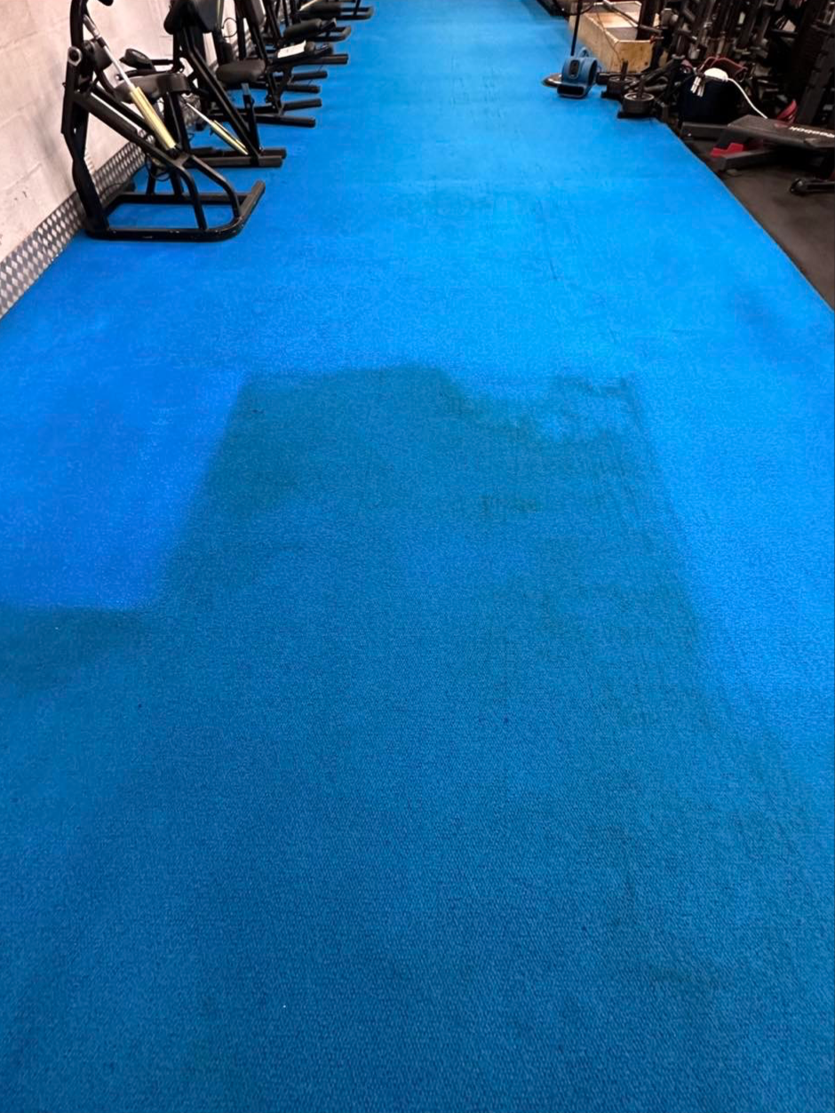 gym cleaning a light blue gym floor with half of it clean and half still dirty and stained. There is gym equipment in the background